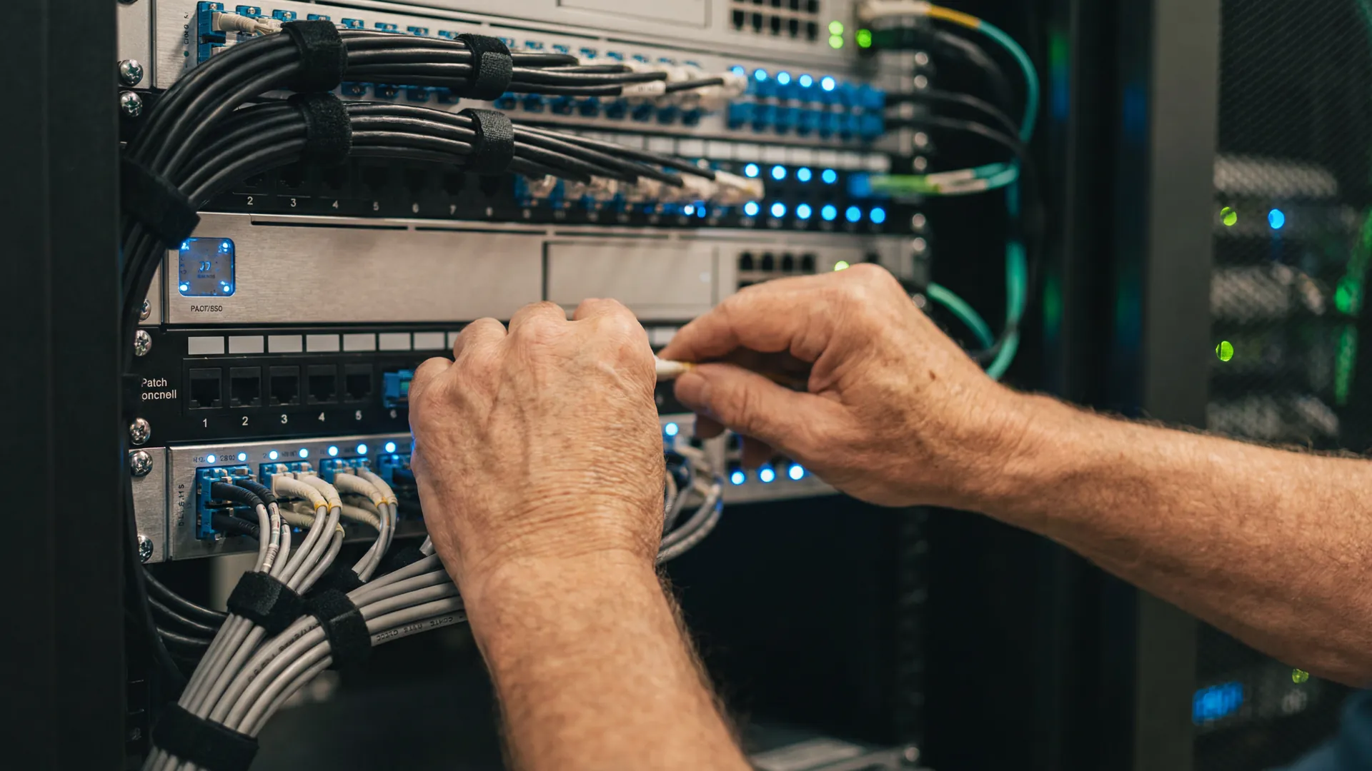 Manos expertas de un ingeniero conectando fibra óptica en un panel de telecomunicaciones